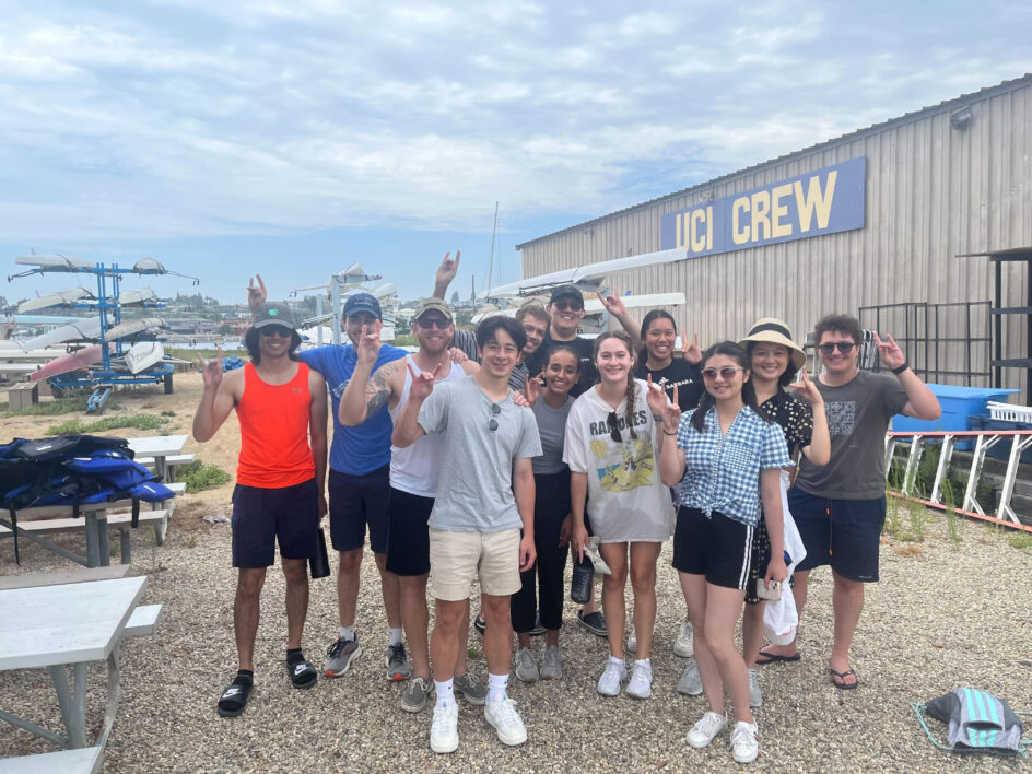 Group photo with a building that says “UCI Crew” and kayaks in the background.