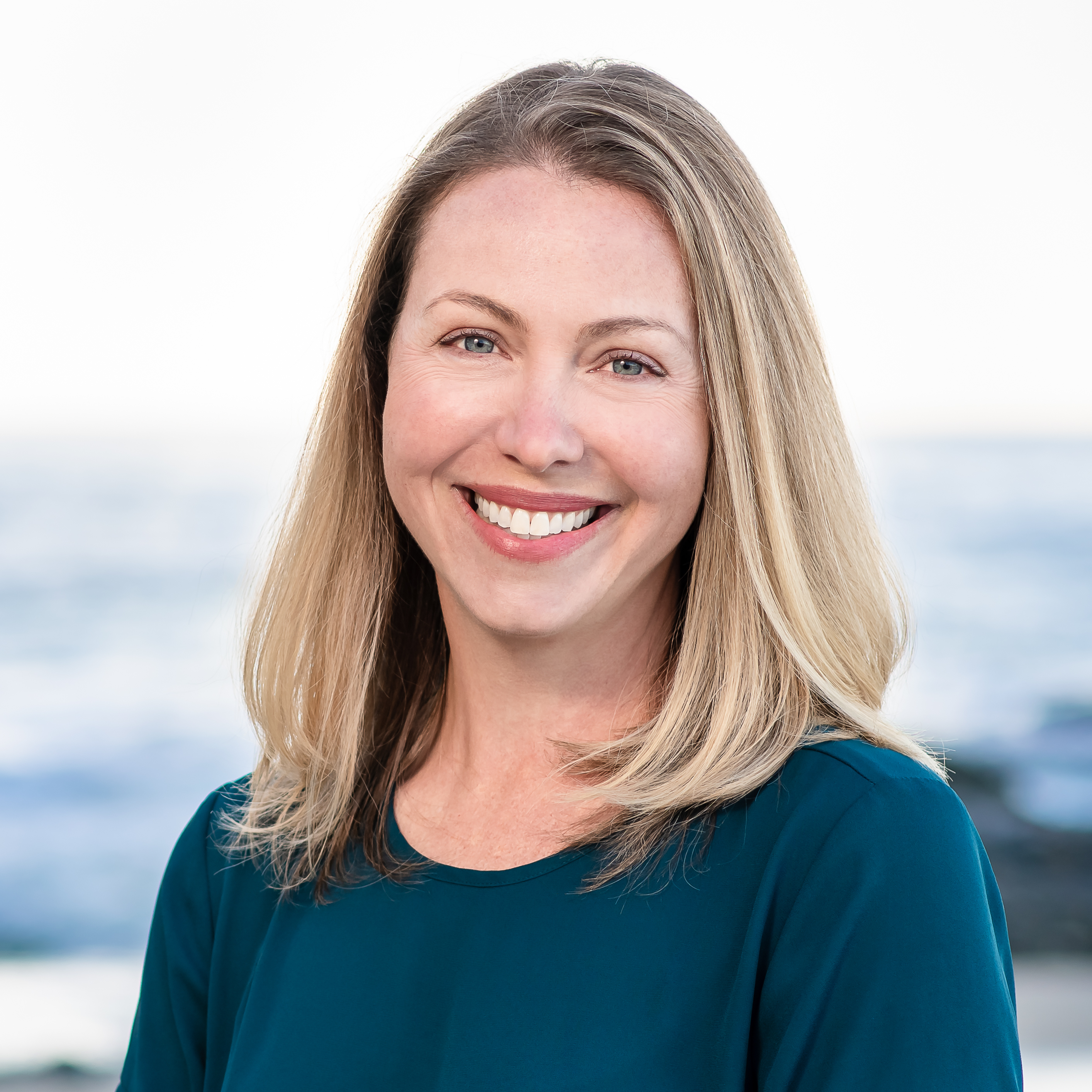 woman with light brown hair smiling and standing in front of ocean